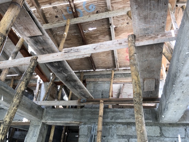 Two layers of bamboo poles hold up the plywood on the roof inside the building.